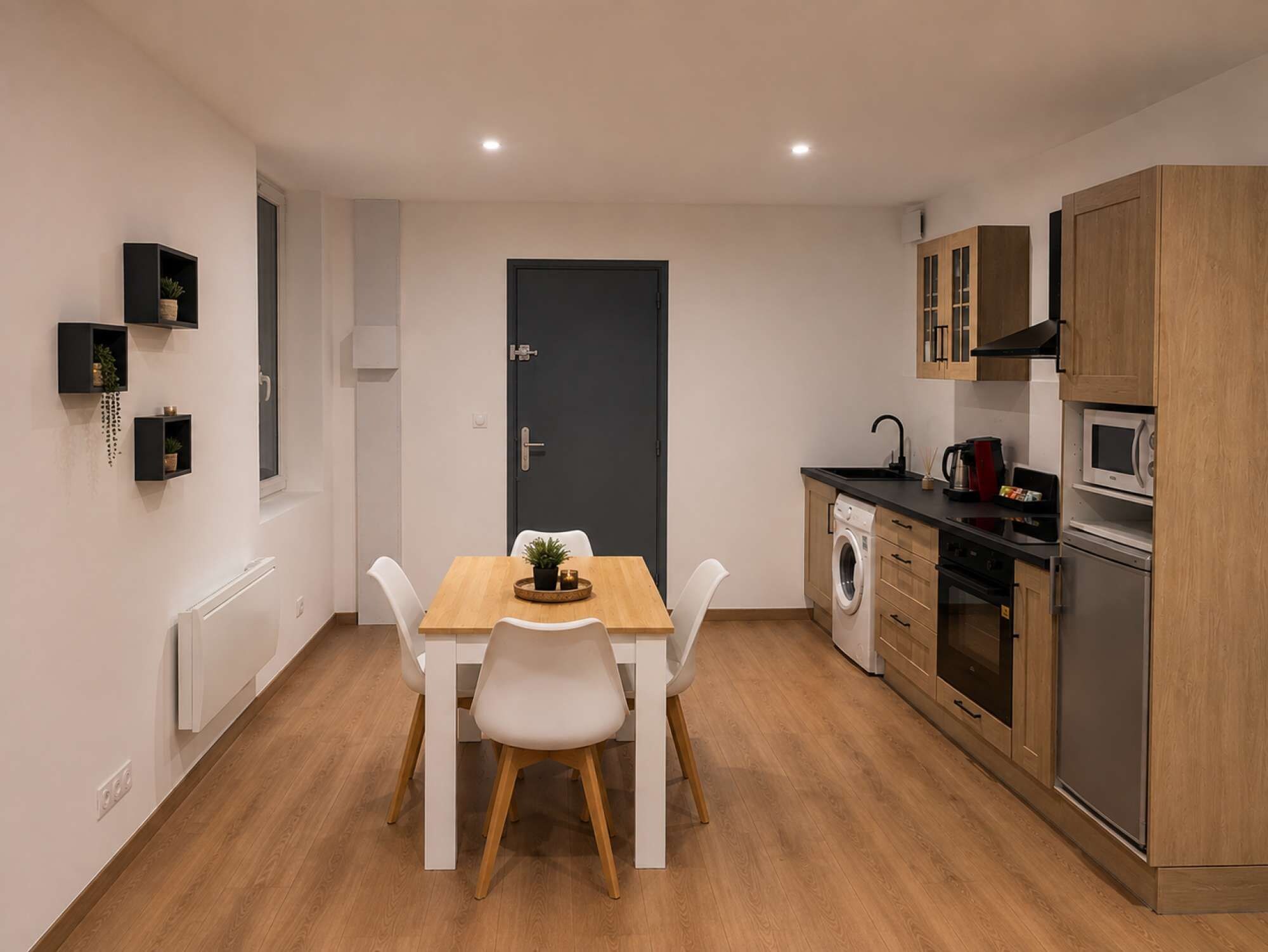 Une cuisine de taille réduite avec une table à manger, des chaises blanches et des meubles de rangement en bois.