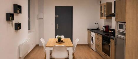 A compact kitchen with a dining table, white chairs, and wooden cabinets.