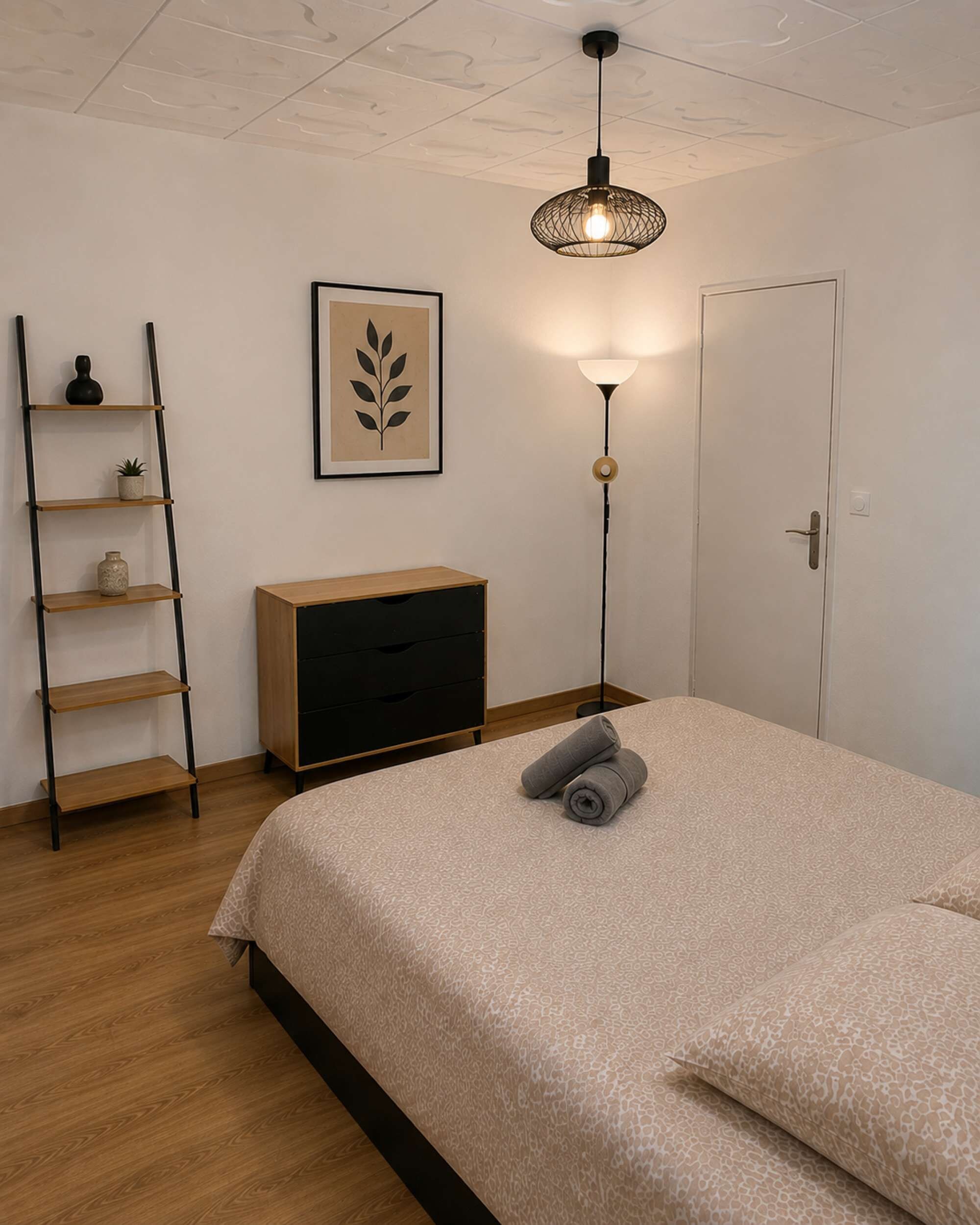 A bedroom with a bed, a bedside table, a floor lamp, a wall-mounted shelf, and a door.