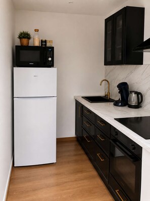 A compact kitchen with a refrigerator, microwave, stove, sink, and black cabinets. - L'Escale d'Iris – A Cozy, Independent Two-Bedroom Apartment in Mazamet (Mazamet)