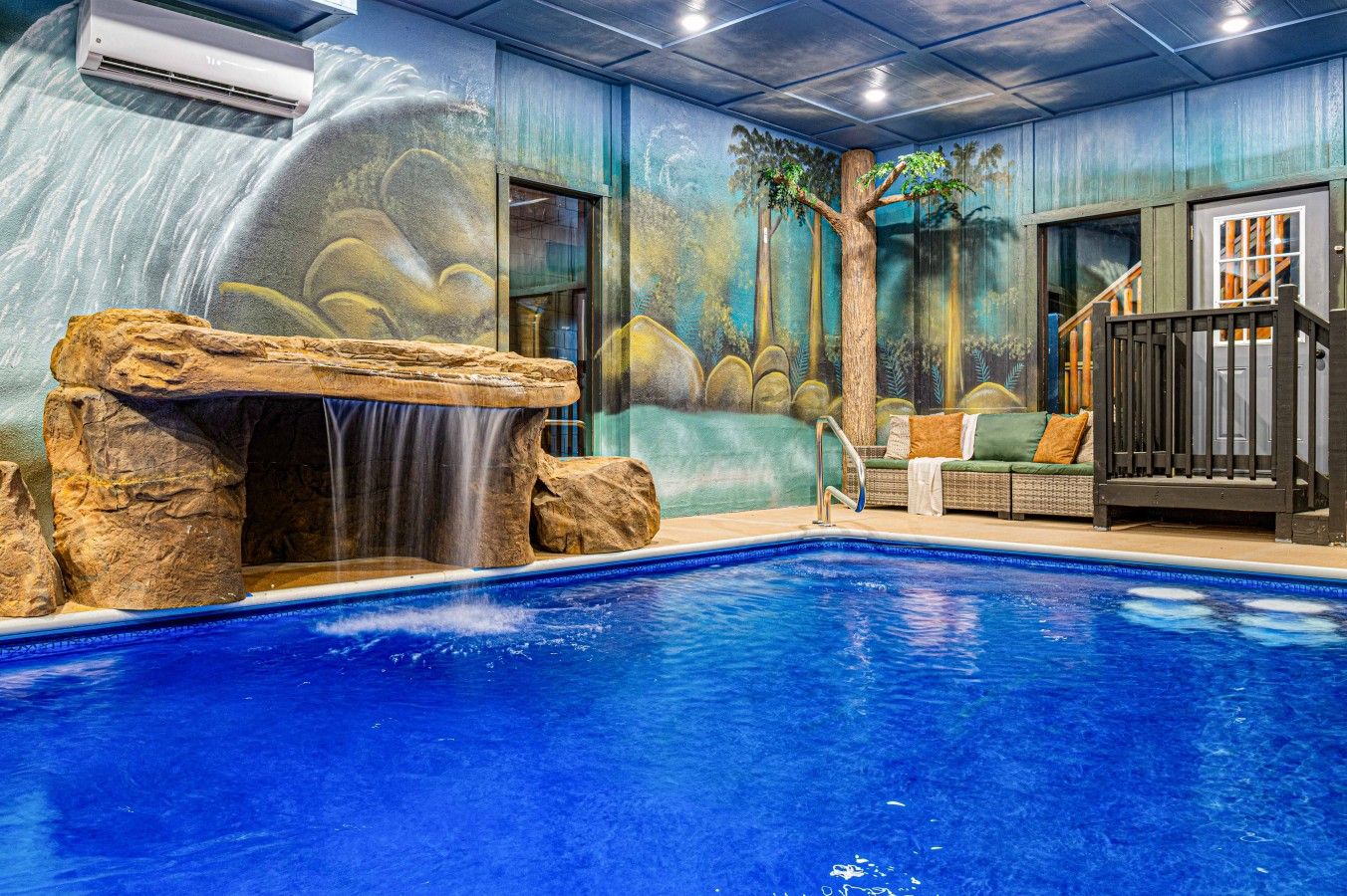 An indoor pool with a waterfall feature, surrounded by a mural of a tropical scene.
