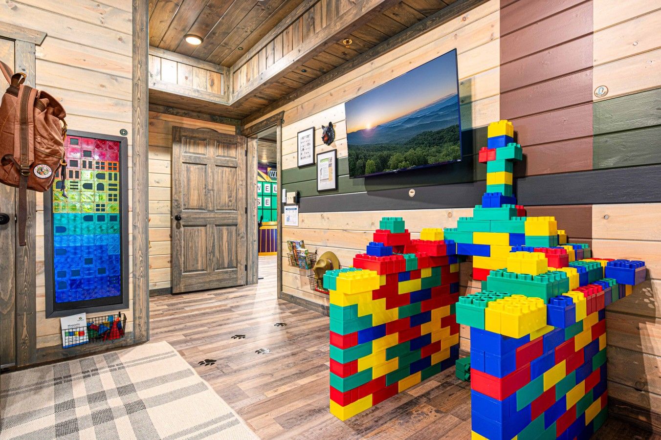 A room with wooden walls, a television mounted on the wall, and colorful building blocks on the floor.