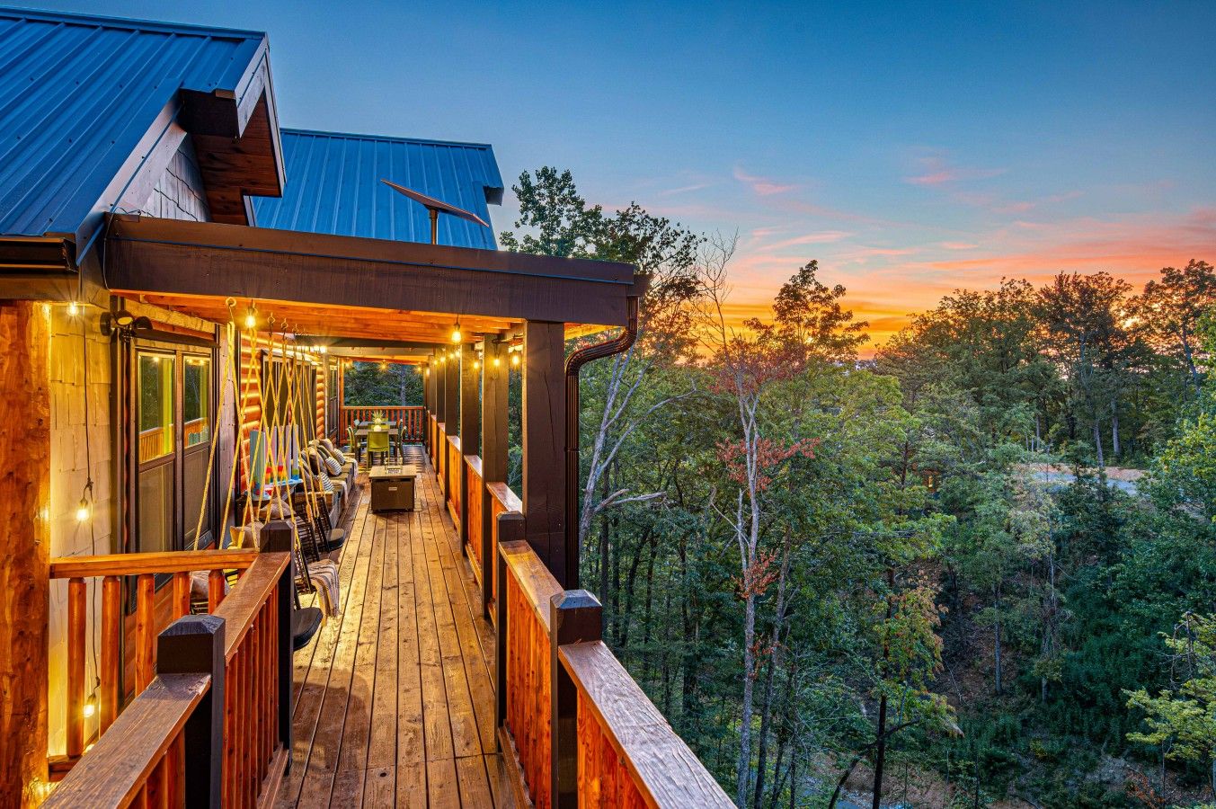 A wooden deck with a railing, a covered seating area, and a view of a forested landscape.