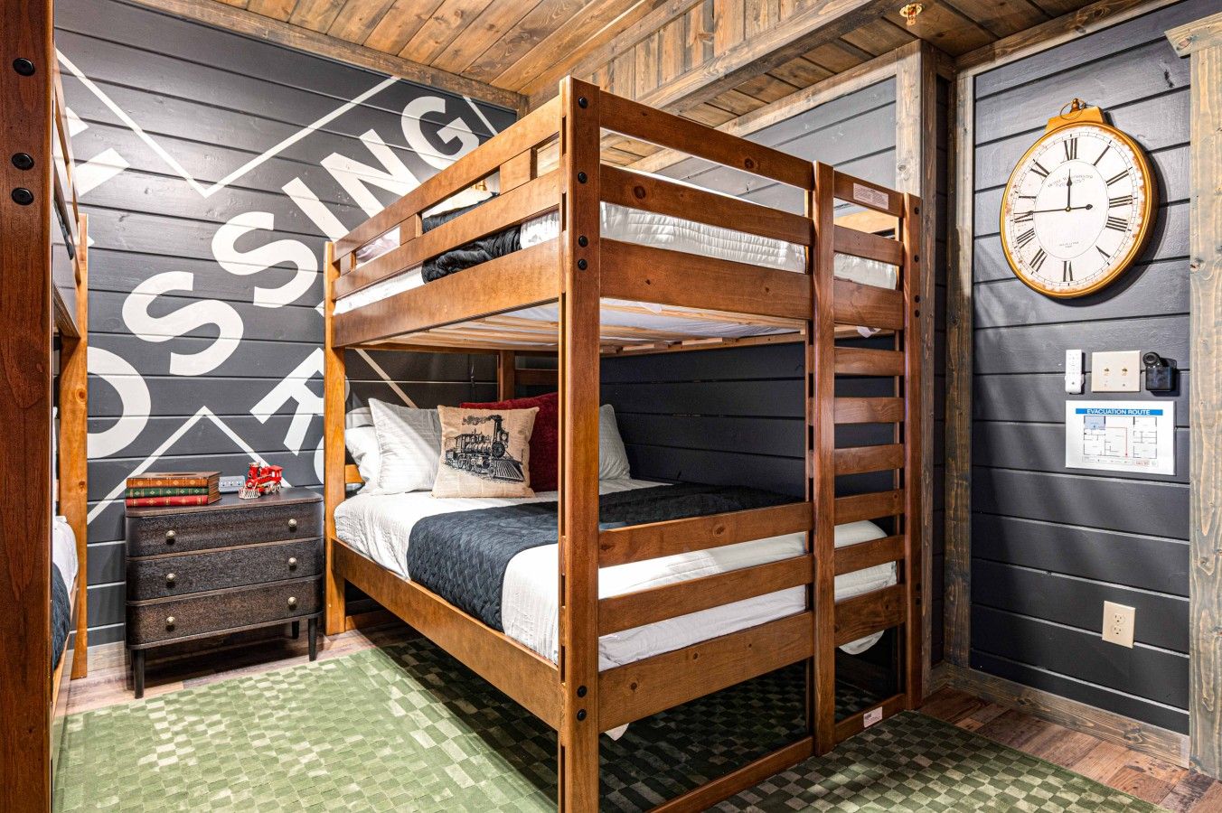 Ein Stockbett mit Holzbettgestell, eine Kommode mit Büchern, eine Uhr und eine Wand mit einer Karte.