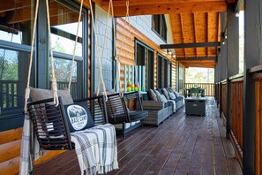 Eine überdachte Veranda mit Holzboden, Sitzgelegenheiten im Freien und großen Fenstern.