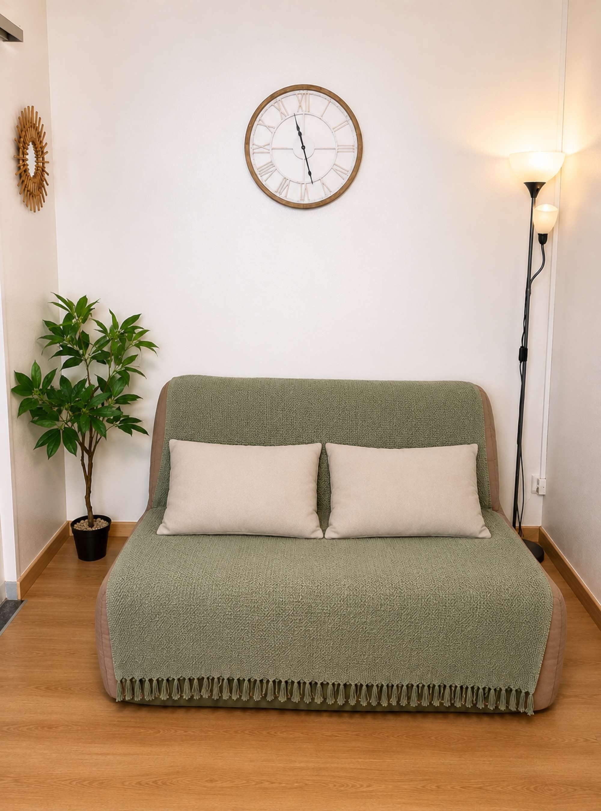 Une pièce avec un canapé vert, une horloge murale, une lampe sur pied et une plante en pot.