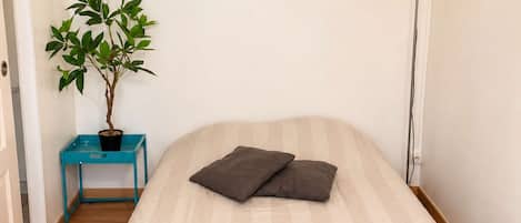 Un dormitorio con una cama, un reloj de pared, una lámpara de pie, una planta en maceta y una mesita.