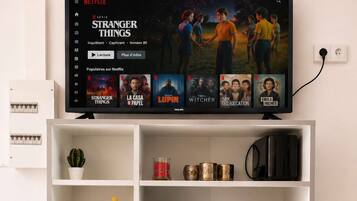 Une étagère blanche sur laquelle est posée une télévision diffusant la série « Stranger Things » de Netflix, ainsi qu’une sélection de livres et d’ustensiles de cuisine.