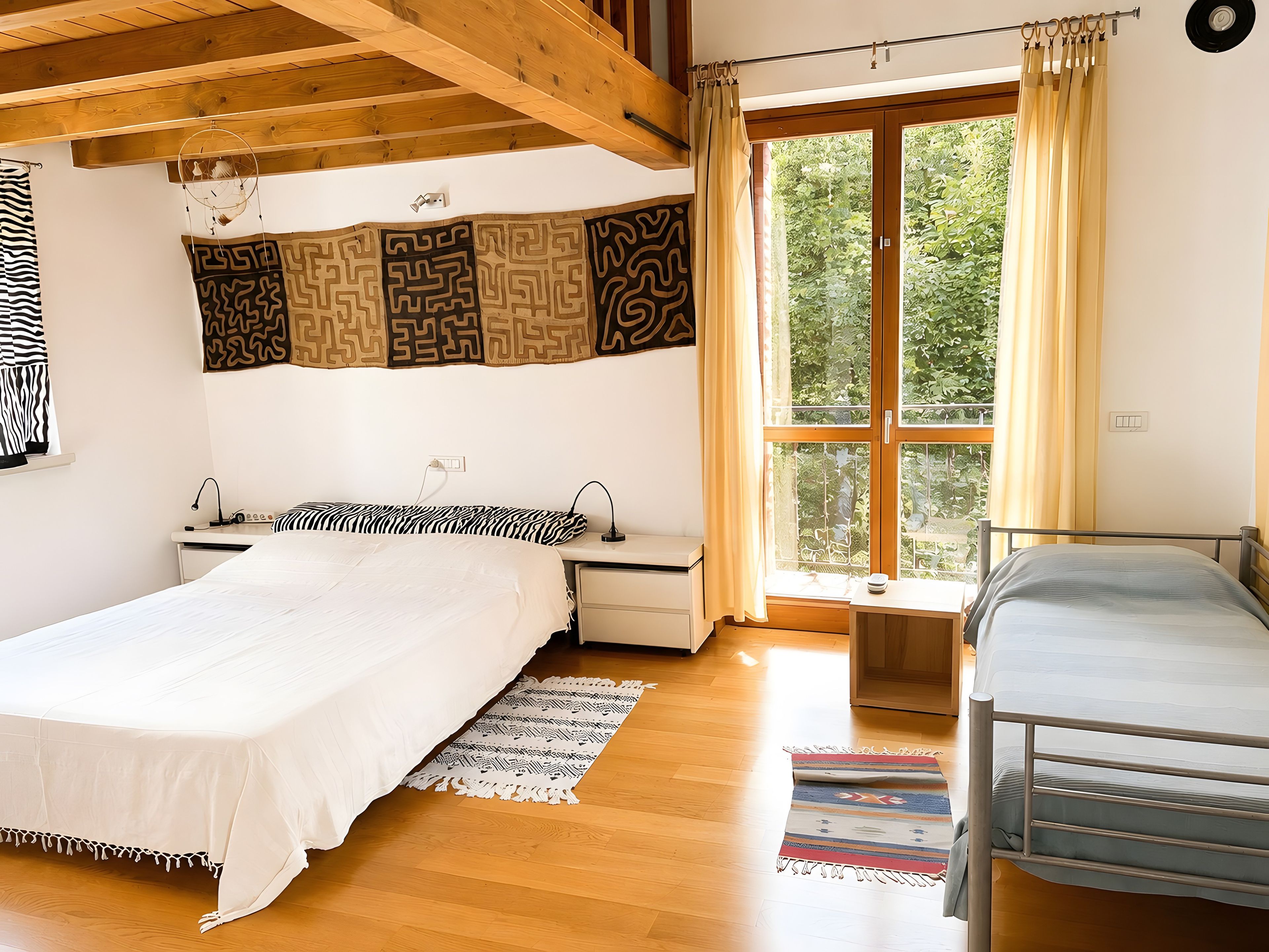 Un dormitorio con una cama grande, una cama más pequeña, un escritorio y una ventana con cortinas.