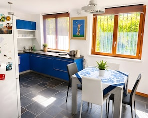 A modern kitchen with blue cabinets, a dining table with chairs, and a window with a view of greenery. - Holiday Home 'Casa Le Sorgenti' with Shared Pool, Shared Garden and Wi-Fi (Cocquio-Trevisago)
