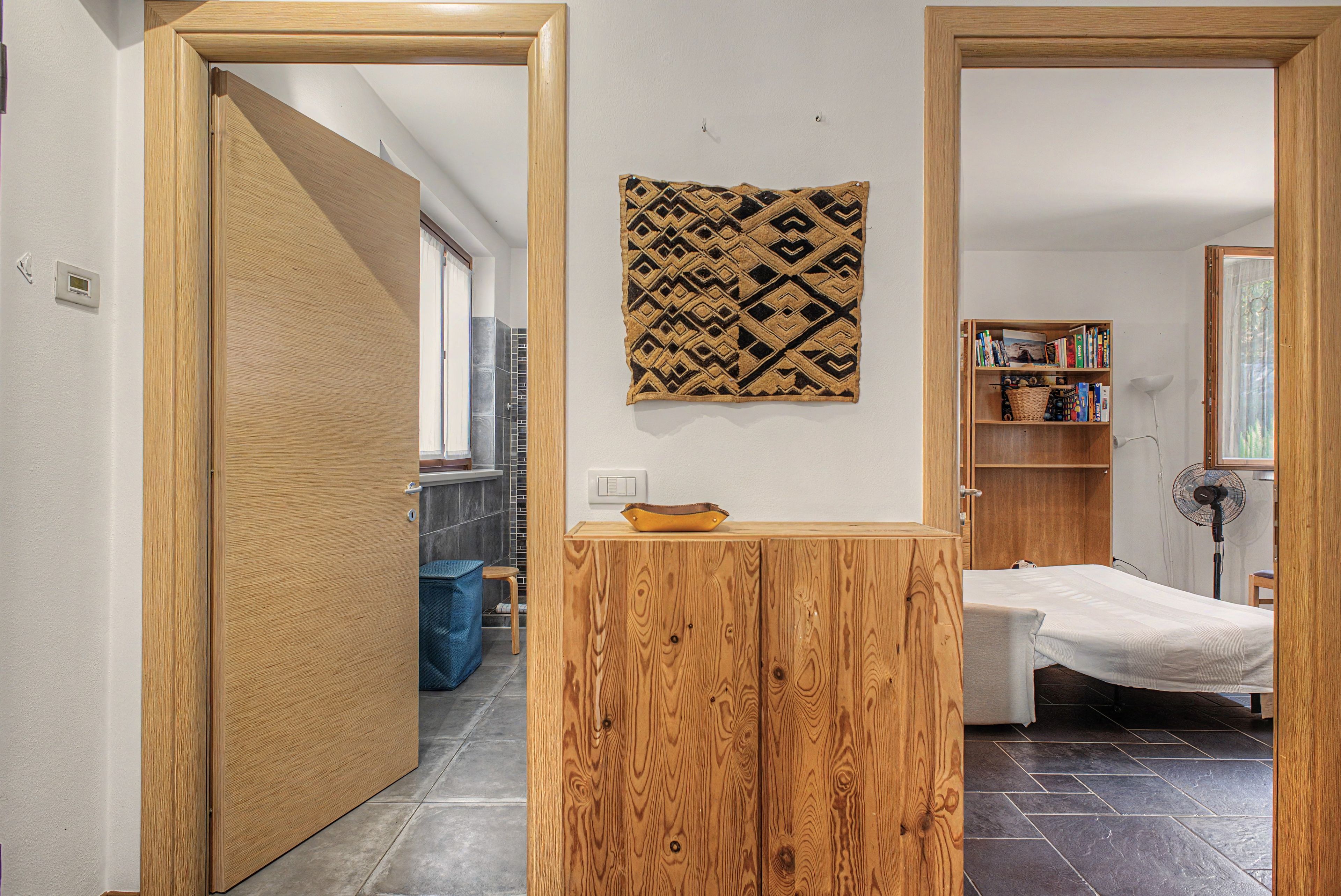 A compact room with a bed, a small table, a bookshelf, and a patterned rug.