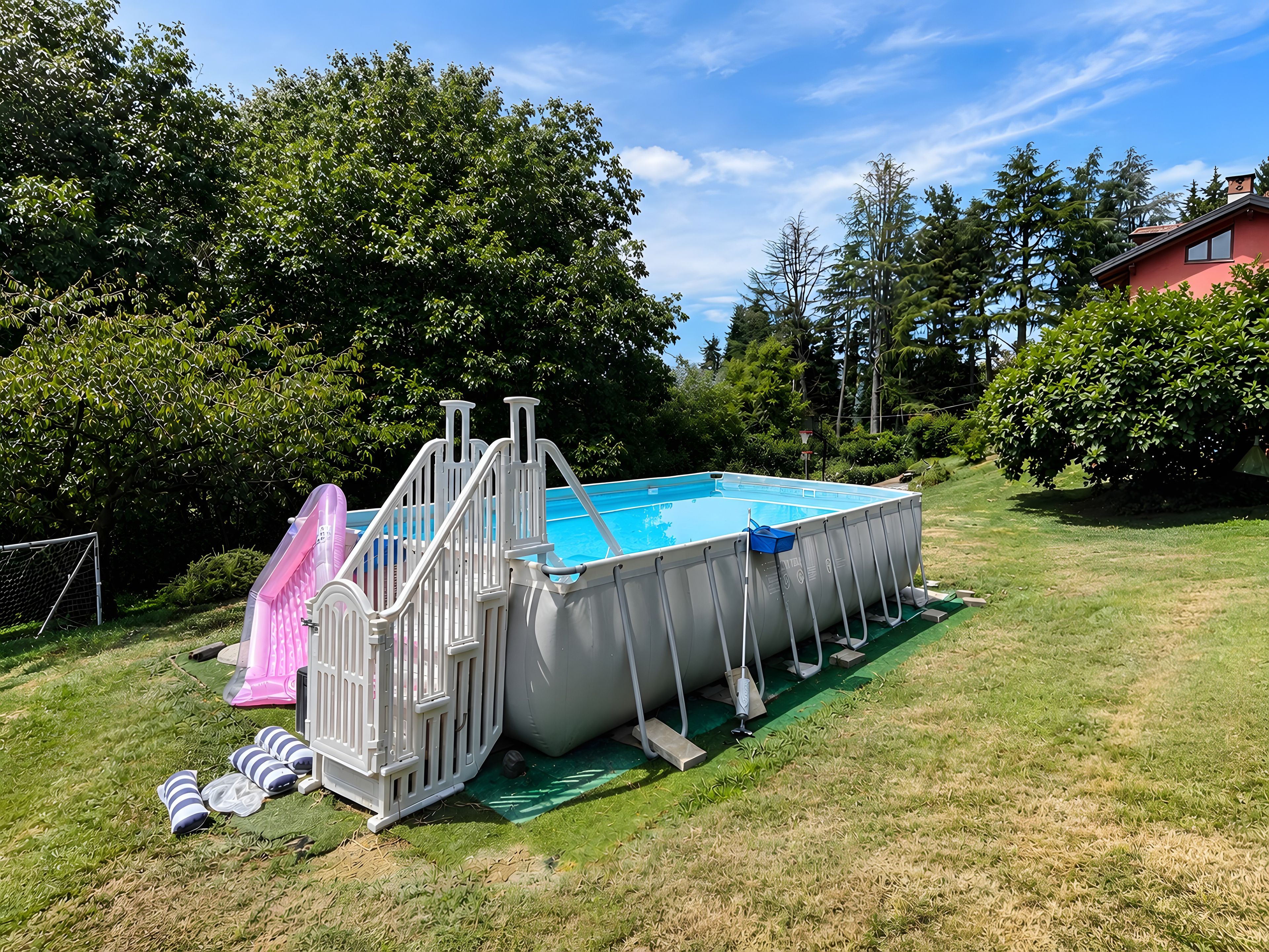 Una piscina elevada con tobogán y vallas de seguridad, rodeada de césped y árboles.