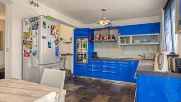Una cocina moderna con armarios azules, un refrigerador de acero inoxidable y una zona de comedor con una mesa y sillas.