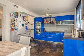 Eine moderne Küche mit blauen Schränken, einem Edelstahlkühlschrank und einem Essbereich mit Tisch und Stühlen.
