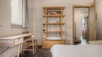 Un dormitorio con cama, escritorio, silla y estantería con toallas y una lámpara.