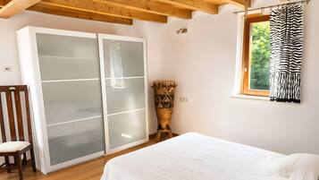A bedroom with a bed, a wooden chair, a wardrobe with frosted glass doors, and a window with a zebra-striped curtain.