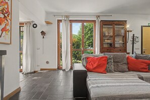 A spacious living room with a large window, a fireplace, and a cozy seating area with cushions.