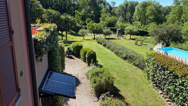 Un jardín ajardinado con piscina, paneles solares y un pequeño pabellón.