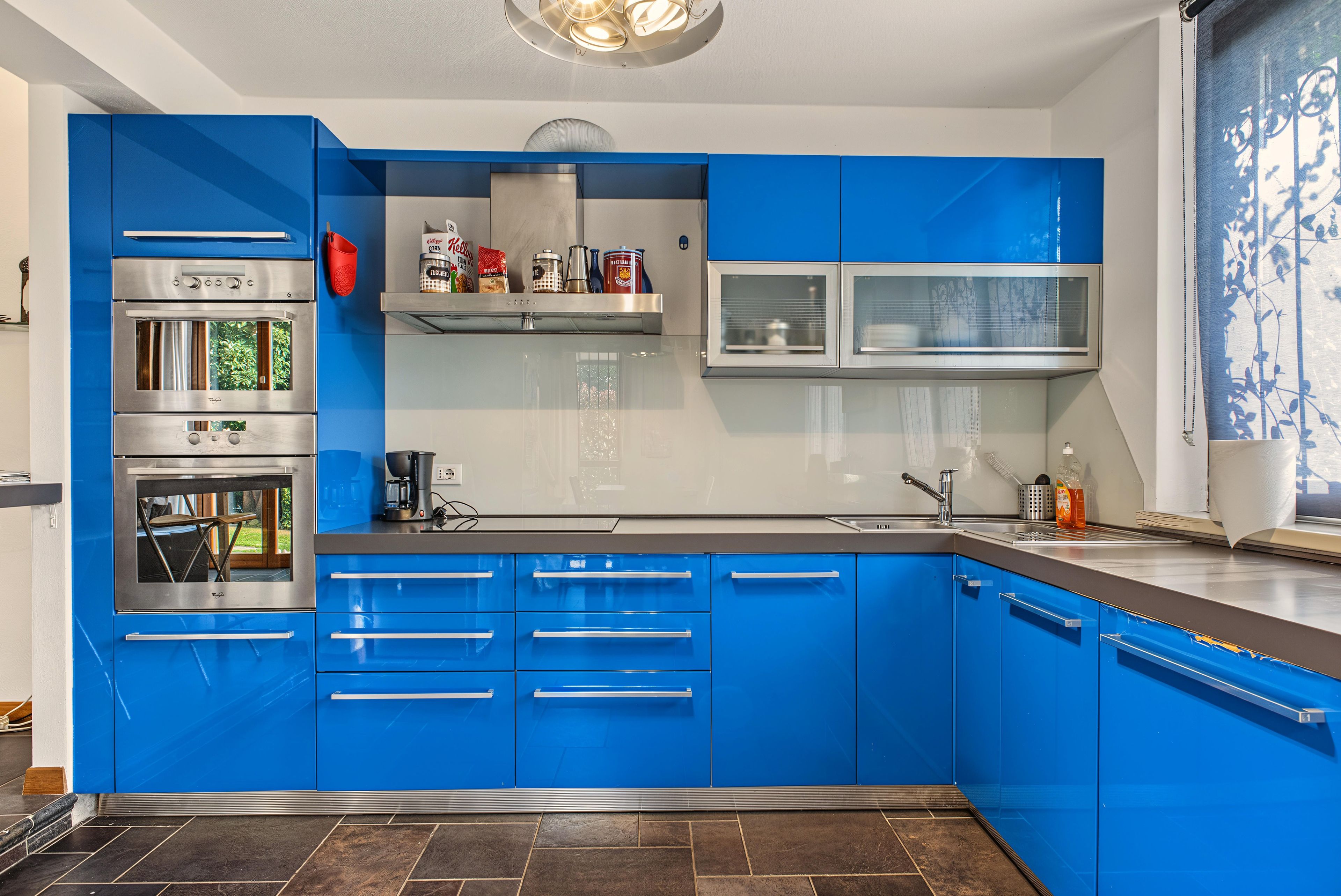 A modern kitchen with blue cabinets, stainless steel appliances, and a window with a view.