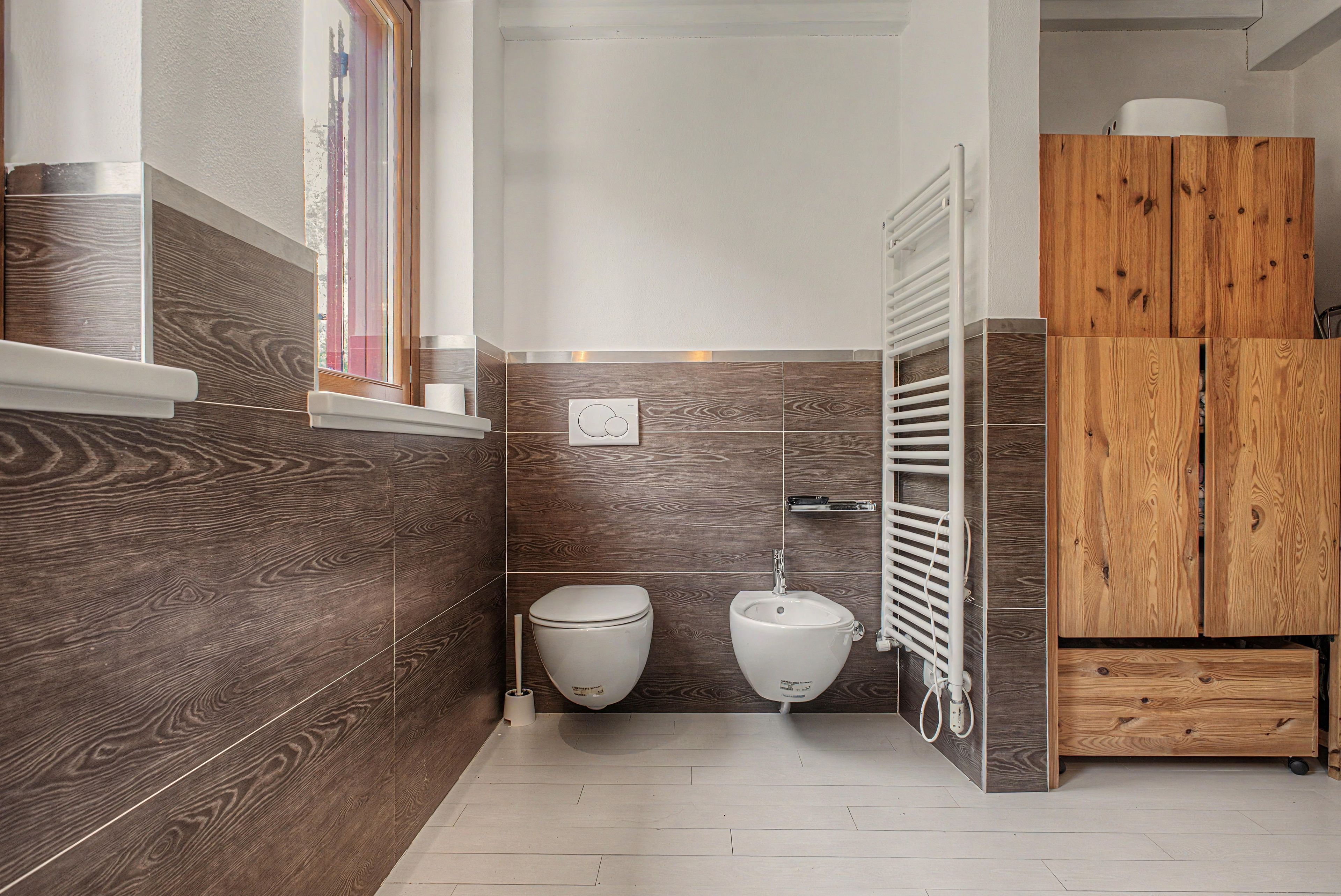 Et moderne badeværelse med toilet, bidet og et træskab.