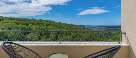 Un balcón con dos sillas y una mesa pequeña, con vistas a un paisaje verde.