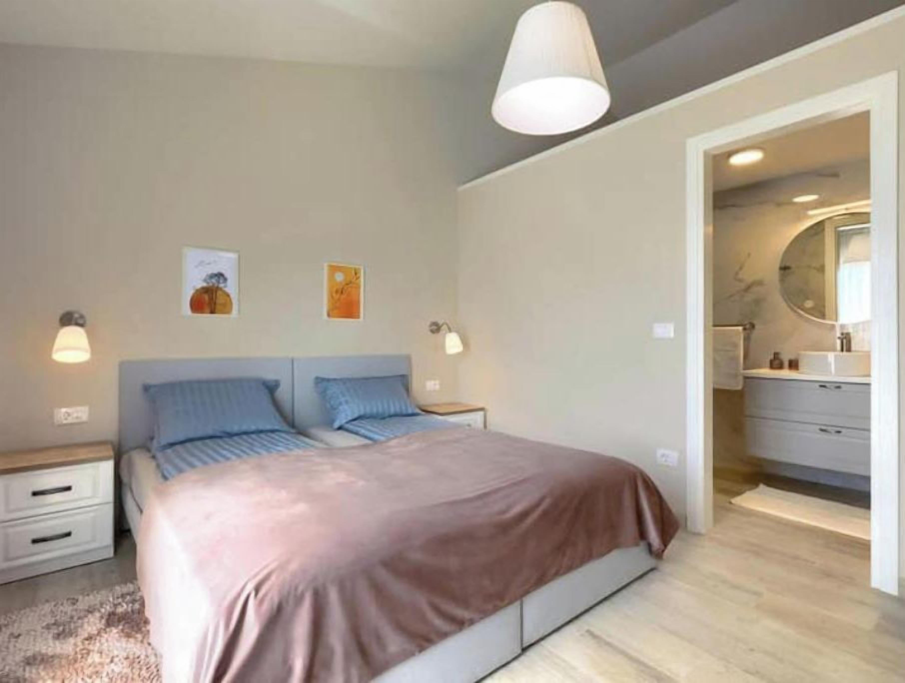 A bedroom with a bed, bedside tables, a nightstand, a dresser, and a bathroom with a mirror.