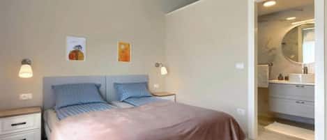 A bedroom with a bed, bedside tables, a nightstand, a dresser, and a bathroom with a mirror.