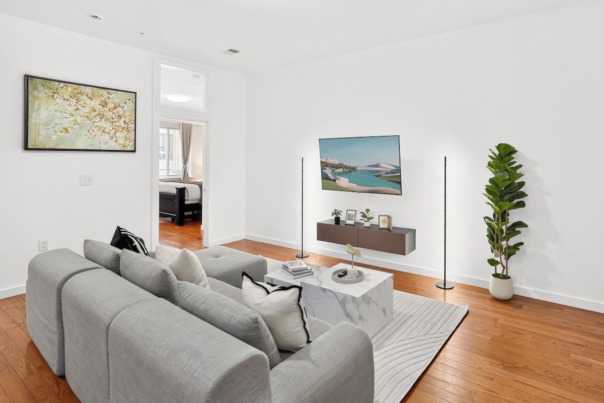 A modern living room with a grey sofa, a marble coffee table, and a large painting on the wall.