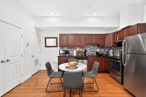 A modern kitchen with wooden cabinets, stainless steel appliances, and a dining area with a round table and four chairs. - A Foodie's Basecamp | 2BR/2BA Center City Philly (Philadelphia)