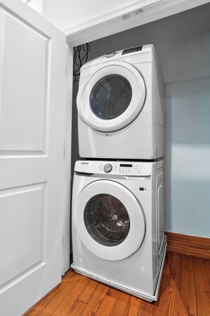 Una columna combinada de rentadora i assecadora en un racó d'una habitació amb sòl de fusta.