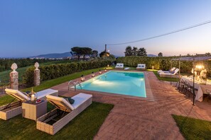 Ein rechteckiger Pool mit einer umlaufenden Terrasse, inklusive Liegestühlen und einer Essgruppe.