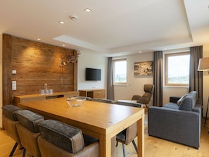 Una sala de estar moderna con una mesa de comedor de madera, sofás grises y un televisor de pantalla plana montado en la pared.