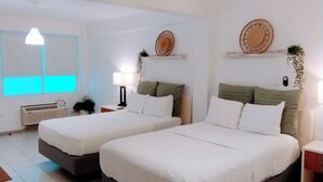 Et hotelværelse med to senge, et natbord med lampe, en vægmonteret hylde med pynteting og et vindue med persienner.
