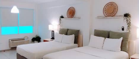 Una habitación de hotel con dos camas, una mesita de noche con lámpara, un estante en la pared con adornos, y una ventana con persianas.