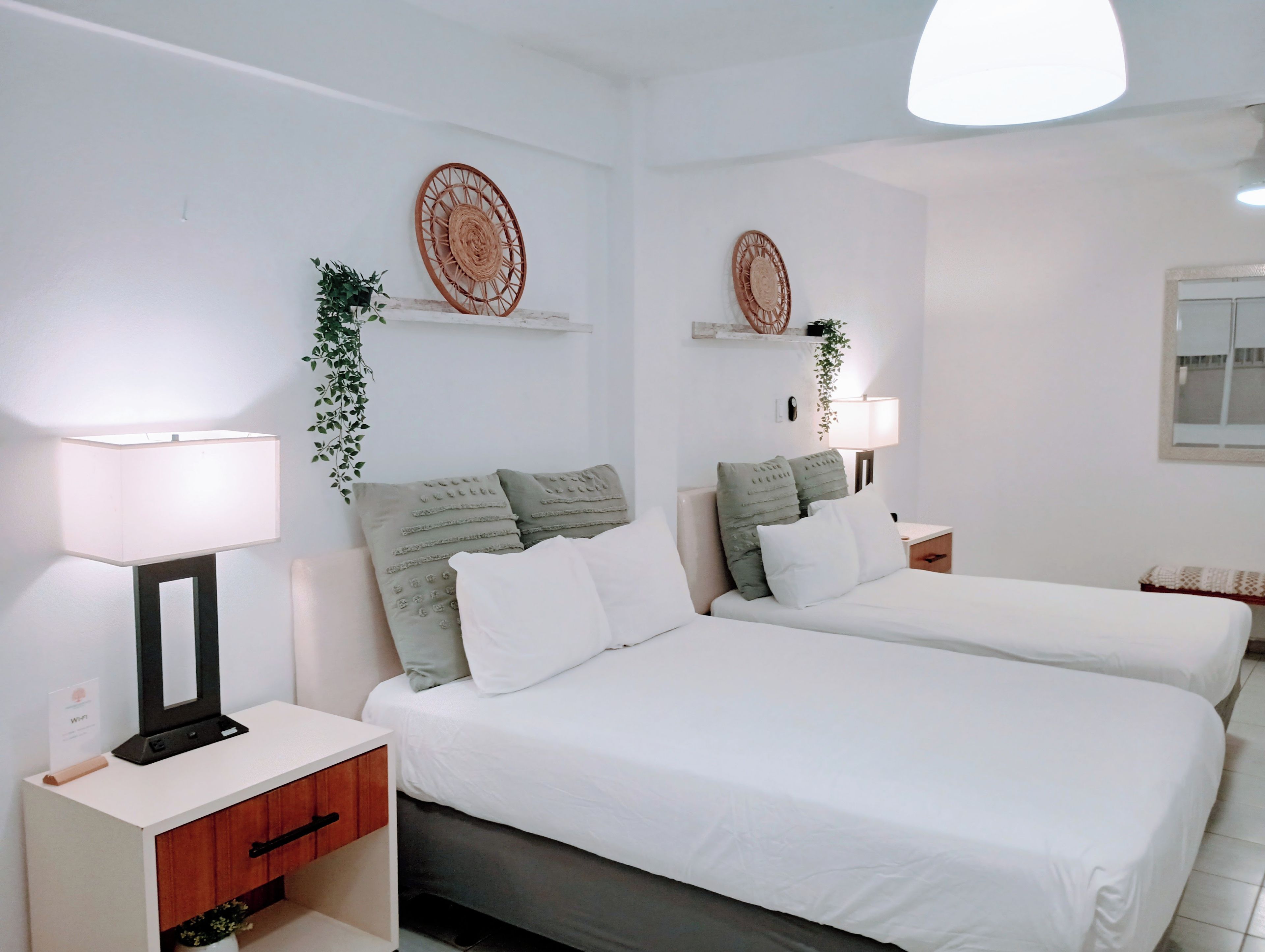 A hotel room with two beds, white bedding, a bedside table with a lamp, a small wooden cabinet, and decorative wall art.