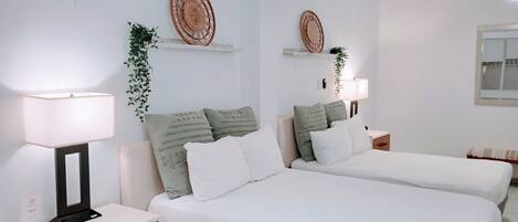 A hotel room with two beds, white bedding, a bedside table with a lamp, a small wooden cabinet, and decorative wall art.