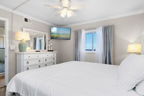 A bedroom with a bed, a dresser, a television mounted on the wall, and a window with curtains. - 6th-Floor Oceanview Condo w/ Beautiful Ocean & Sunrise Views (Emerald Isle)