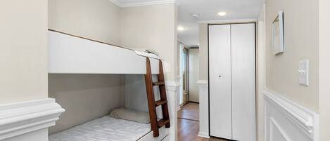 A bedroom with a bunk bed, a wooden ladder, a white door, and a hallway leading to another room.