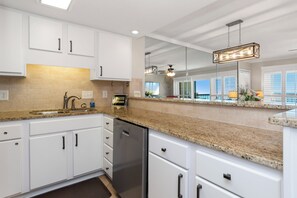 A modern kitchen with white cabinets, granite countertops, and stainless steel appliances. - 6th-Floor Oceanview Condo w/ Beautiful Ocean & Sunrise Views (Emerald Isle)