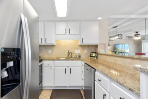 A modern kitchen with white cabinets, a granite countertop, stainless steel appliances, and a built-in oven. - 6th-Floor Oceanview Condo w/ Beautiful Ocean & Sunrise Views (Emerald Isle)