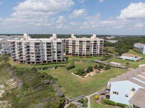 A modern apartment complex with multiple floors, balconies, and a swimming pool. - 6th-Floor Oceanview Condo w/ Beautiful Ocean & Sunrise Views (Emerald Isle)