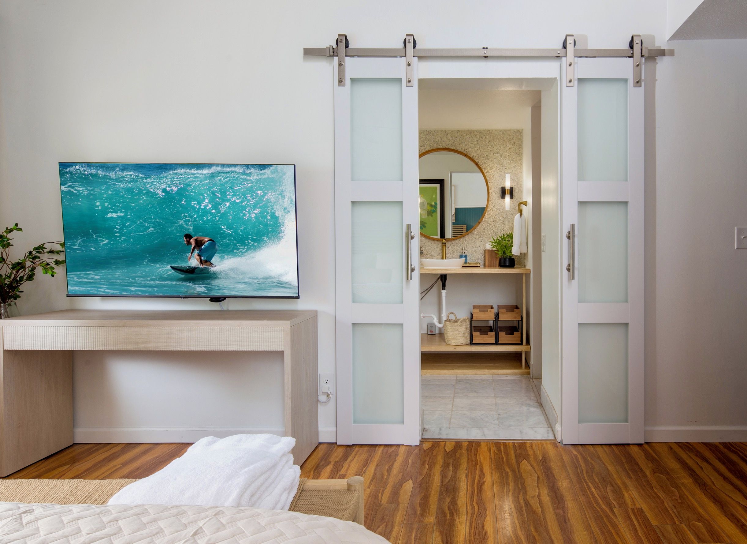 A bedroom with a bed, a TV displaying a surfer, and a sliding door leading to a bathroom.