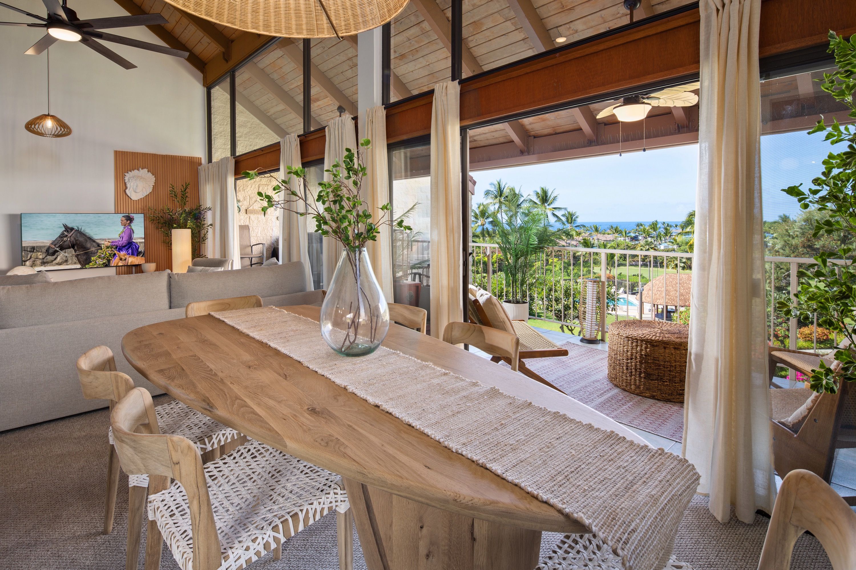 Un espace repas avec une table en bois, des chaises en osier et une vue sur l’océan.