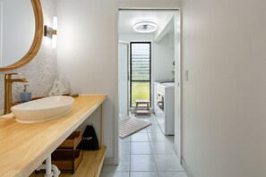 Een moderne badkamer met een grote ovaal wastafel, een ronde spiegel en een houten opbergmeubel.