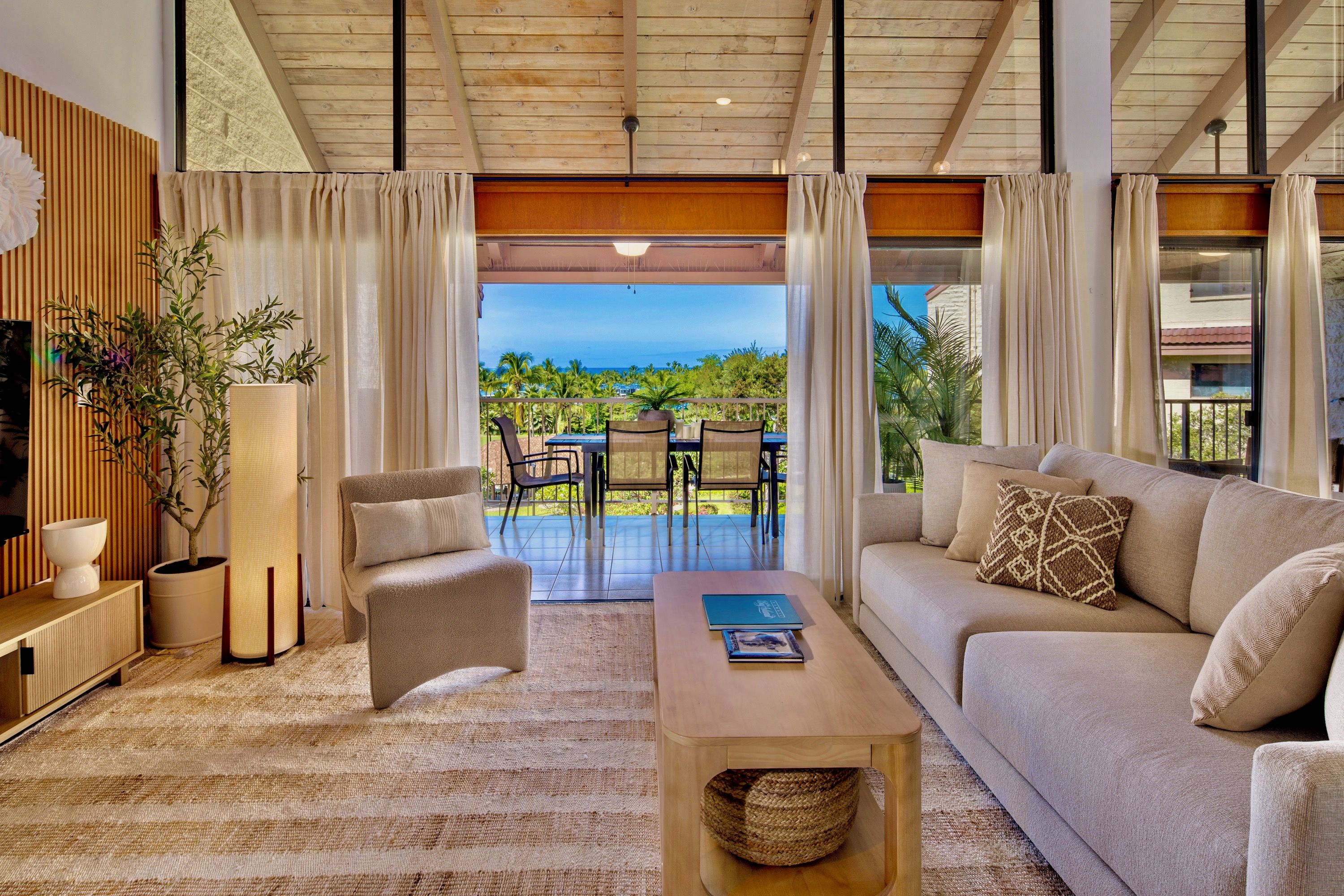 A spacious living area with a sofa, armchair, and coffee table, a television, and a view of the ocean.
