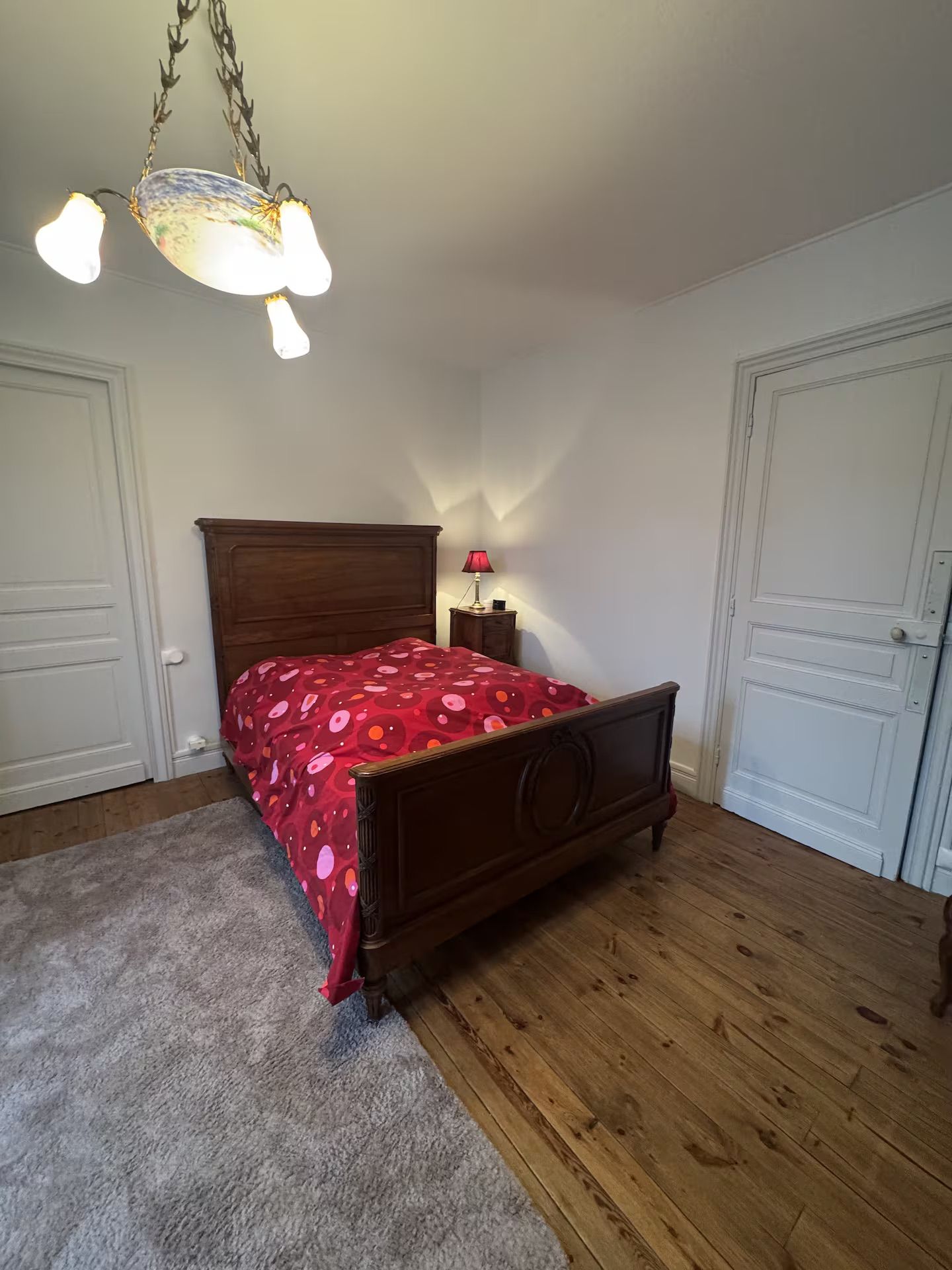 Une chambre à coucher avec un lit en bois, une couvre-lit rouge à motifs, un luminaire suspendu et une table de chevet avec une lampe.