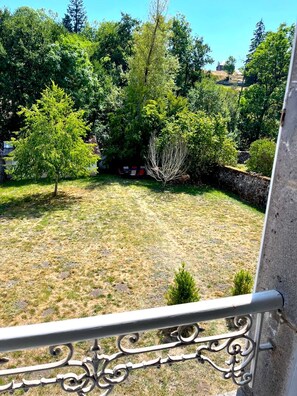 A balcony with a view of a grassy yard, trees, and a stone wall. - Maison Dellac – Les clés du temps (Saint-Saturnin)