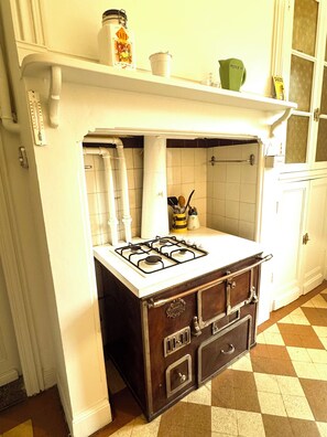 A kitchen with a gas stove, white cabinets, a tiled backsplash, and a checkered floor pattern. - Maison Dellac – Les clés du temps (Saint-Saturnin)