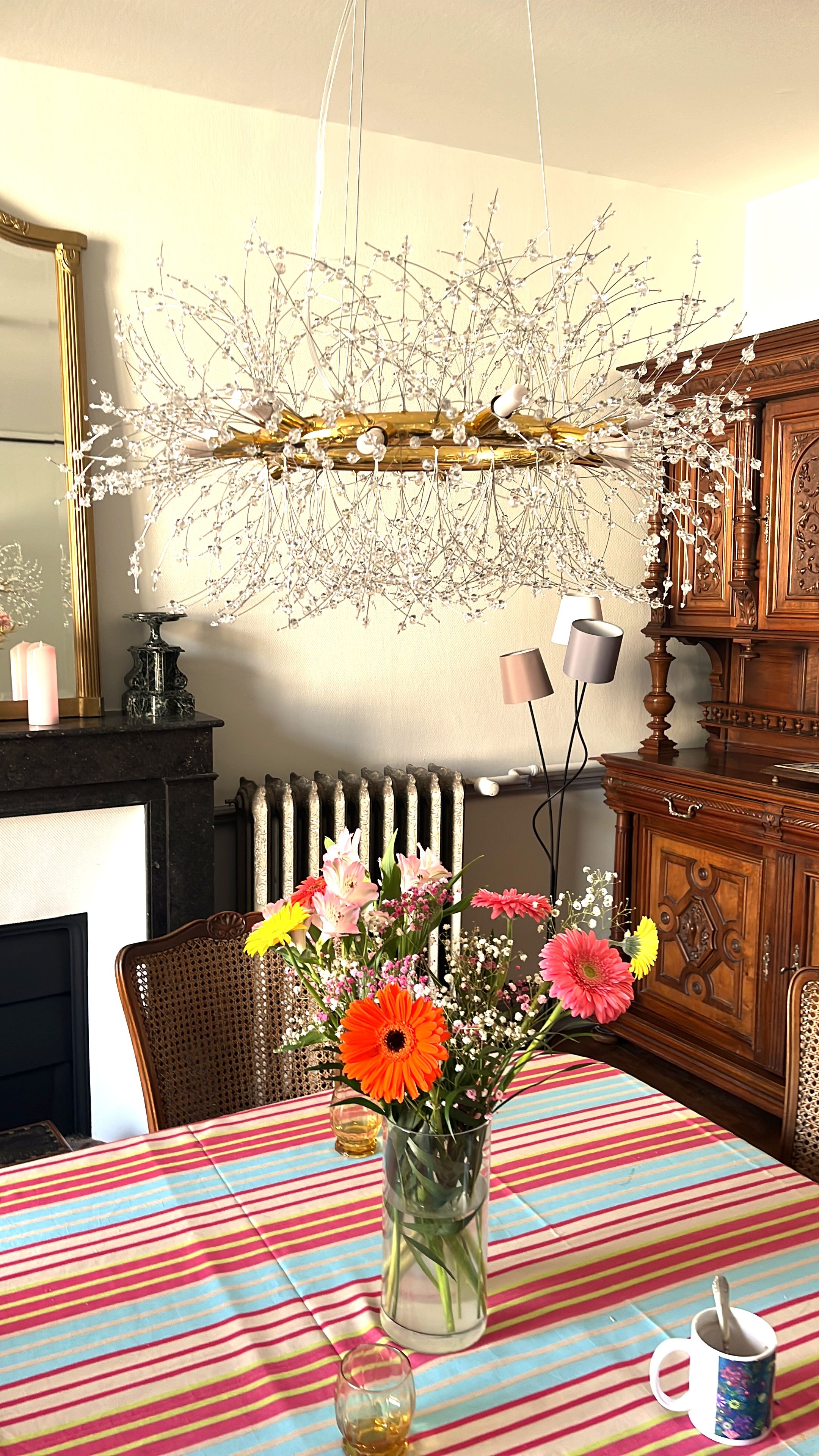 Une table à manger recouverte d’une nappe à rayures, un vase avec des fleurs, une bougie et une tasse.