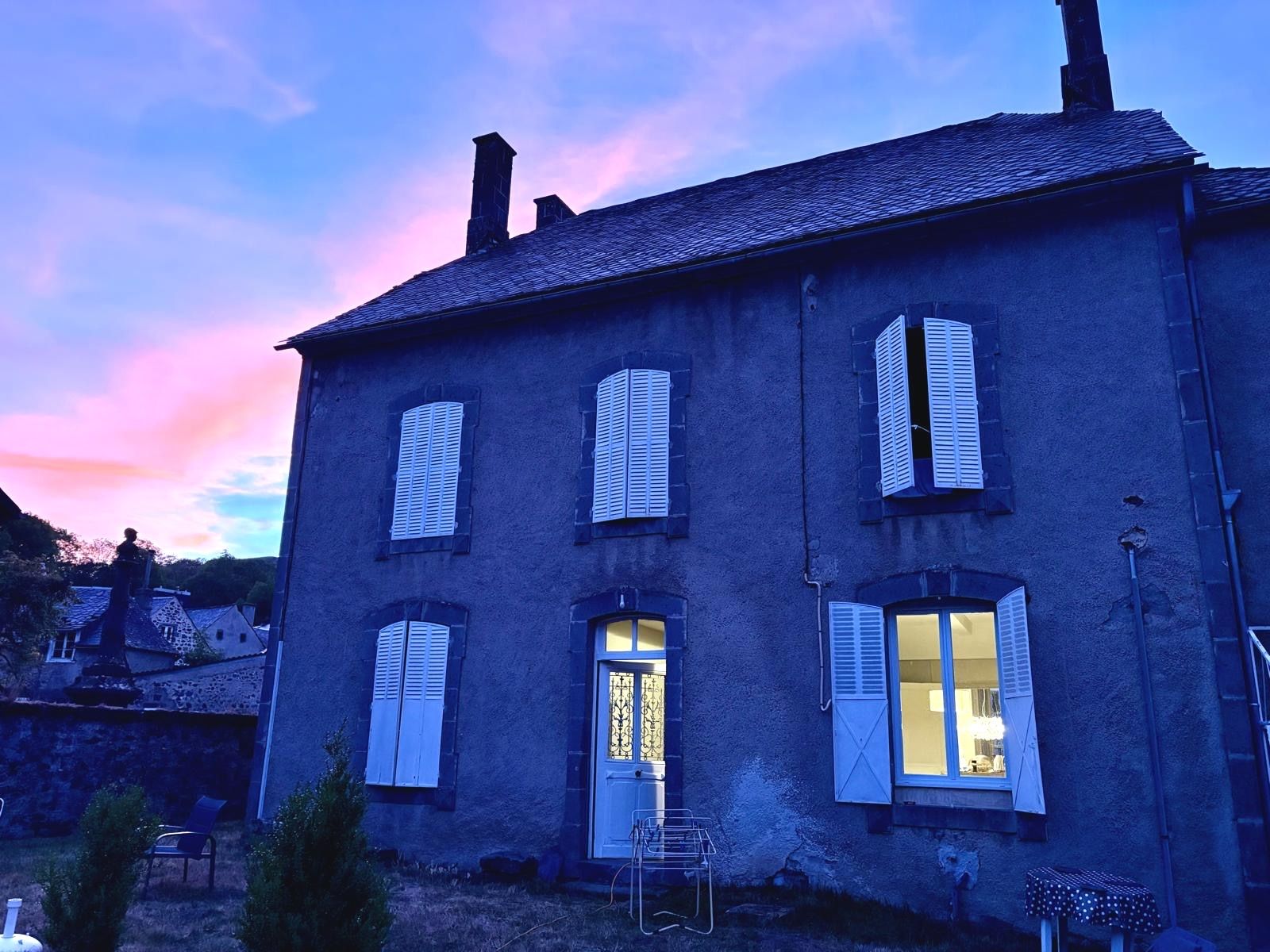 A two-story building with multiple windows and a door, surrounded by a small garden area.